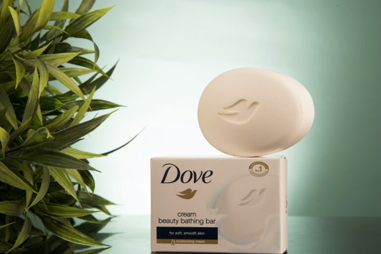 A photo-style image of Dove beauty bar soap displayed in a clean bathroom setting, representing gentle cleansing for sensitive scalp and skin. The image visually supports an article explaining that Dove soap may help reduce scalp irritation but does not treat or prevent hair loss.