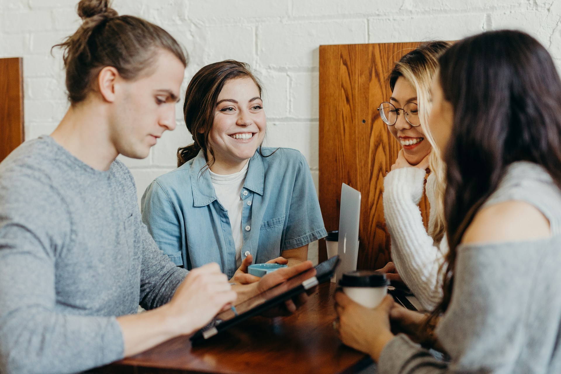 A group of employees collaborating and smiling around a table with laptops and coffee, representing employee happiness, teamwork, and positive workplace culture.