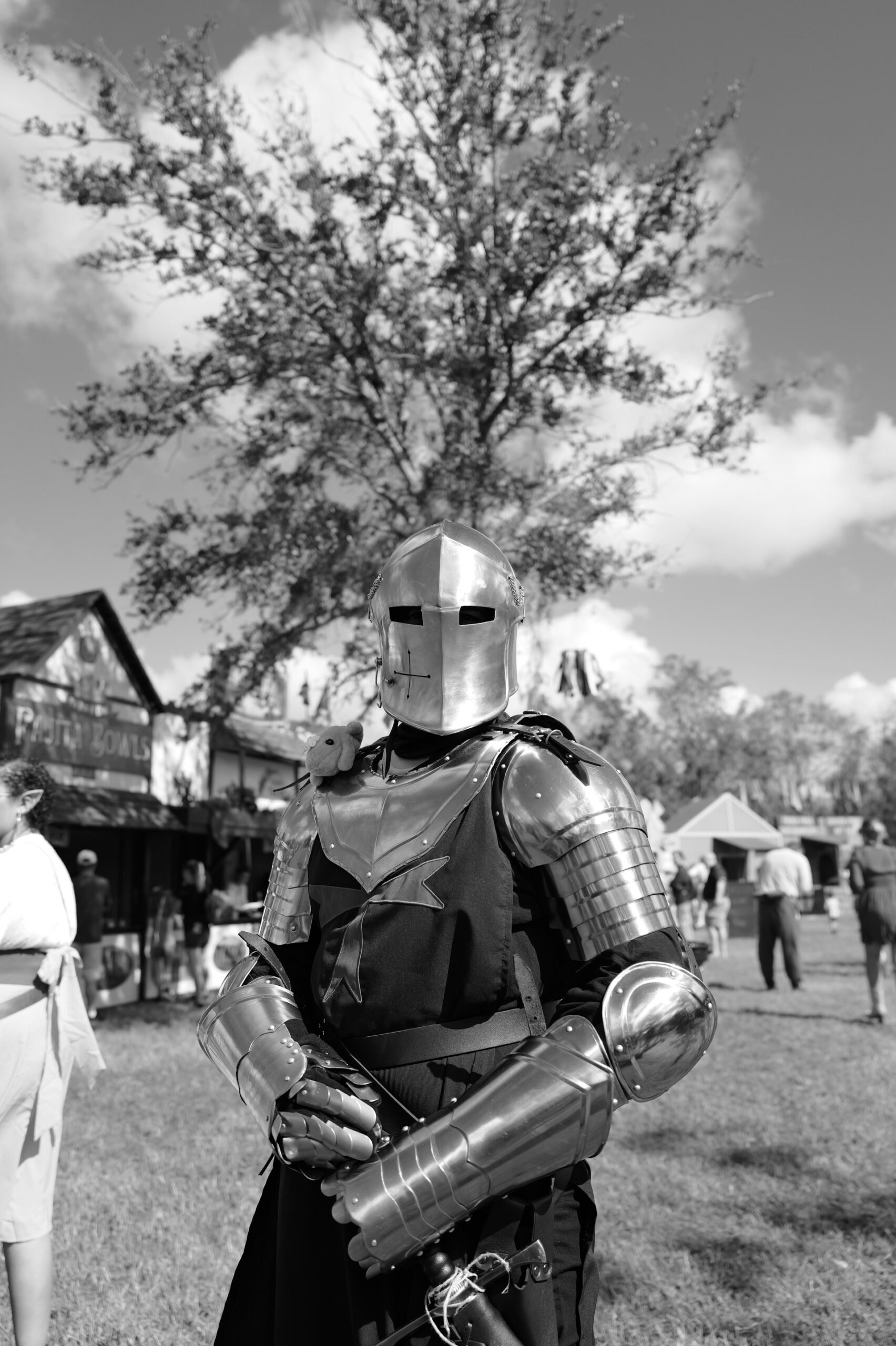 A person wearing full medieval armor stands outdoors at a historical reenactment event, symbolizing strength, protection, and readiness for battle.