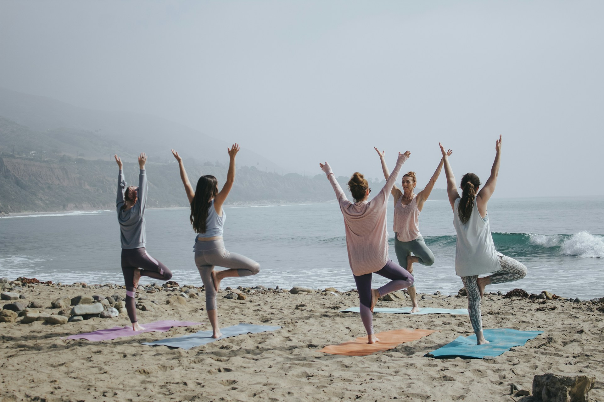 A group of women practicing yoga on the beach in tree pose, promoting heart health, stress relief, and a healthy lifestyle by the ocean.