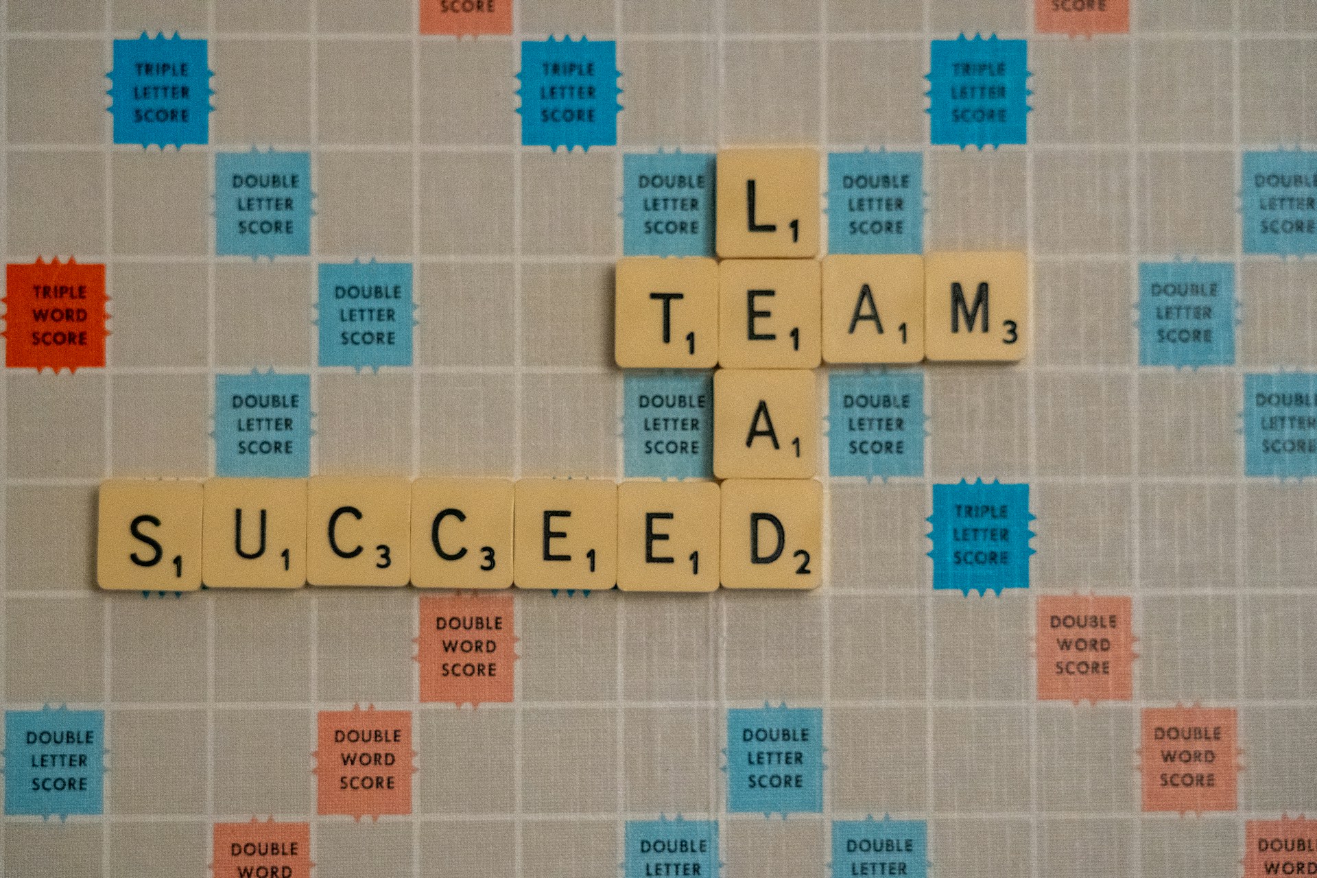 Scrabble board spelling ‘TEAM’, ‘LEAD’, and ‘SUCCEED’, symbolizing teamwork, leadership, and successful strategy execution.