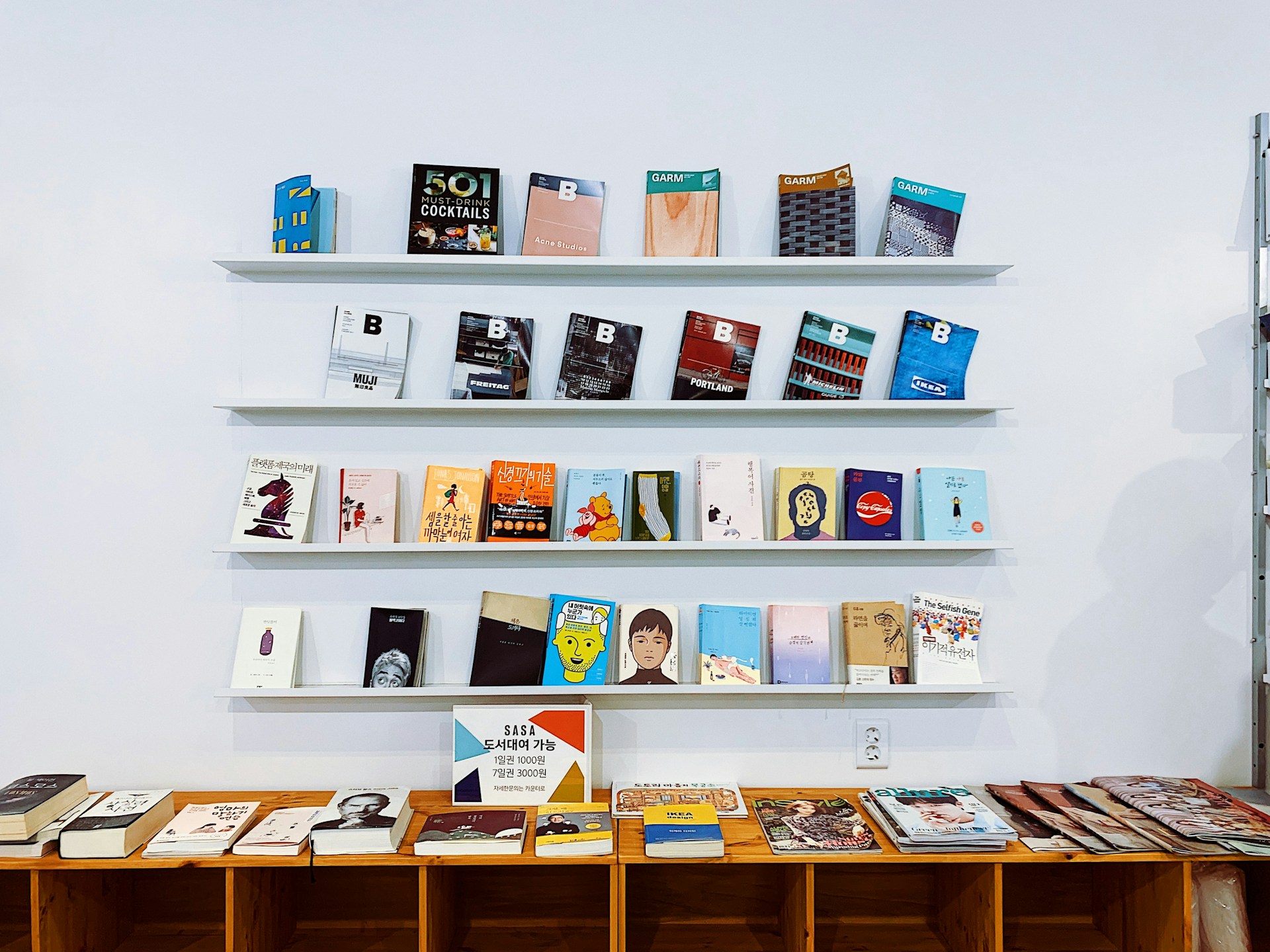 A curated display of books on minimalist white shelves inside an independent bookstore, reflecting the warm and thoughtful atmosphere of Korea’s small publishers like MUZE, where diverse literary voices and creative works are highlighted.