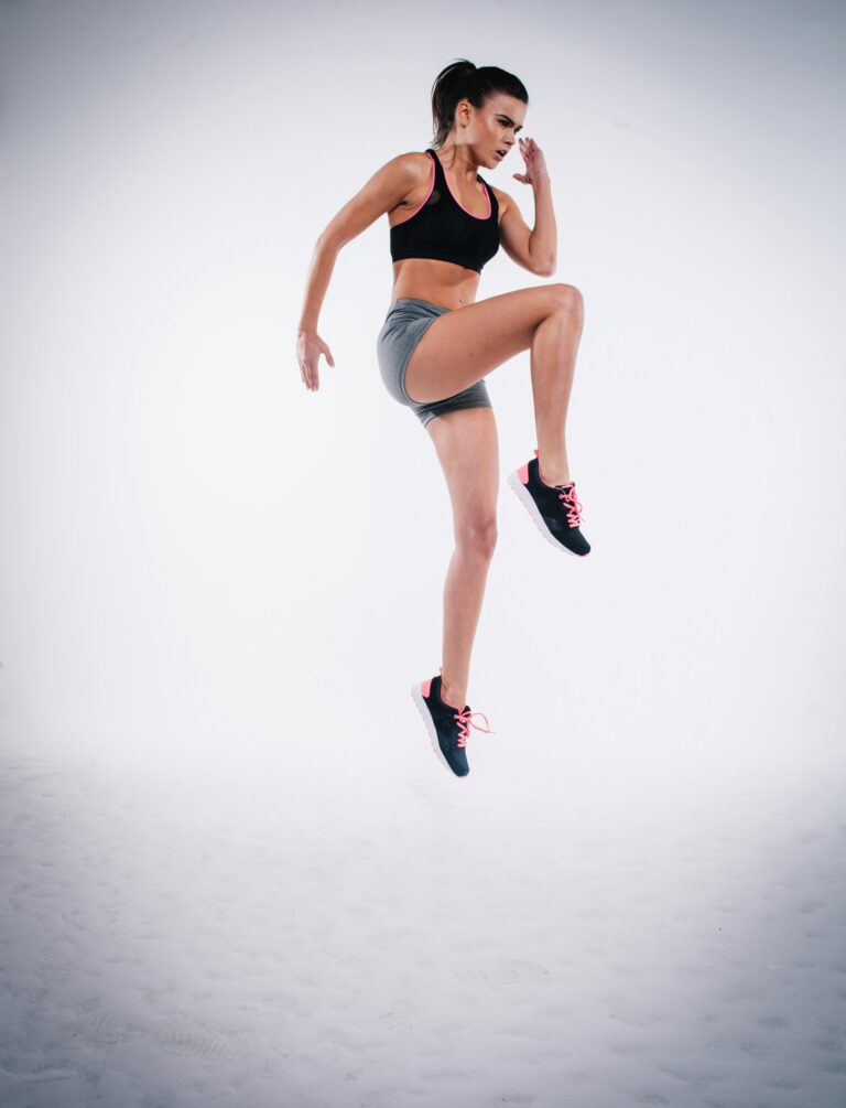 A fit woman performing a high-knee jumping exercise against a clean white background, illustrating a simple morning workout routine to boost energy and circulation.
