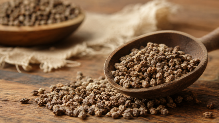 Whole and ground Grains of Paradise spice displayed with ginger and a wooden scoop in a natural kitchen setting.