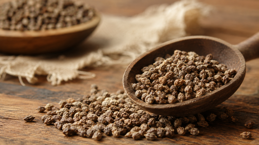 Whole and ground Grains of Paradise spice displayed with ginger and a wooden scoop in a natural kitchen setting.